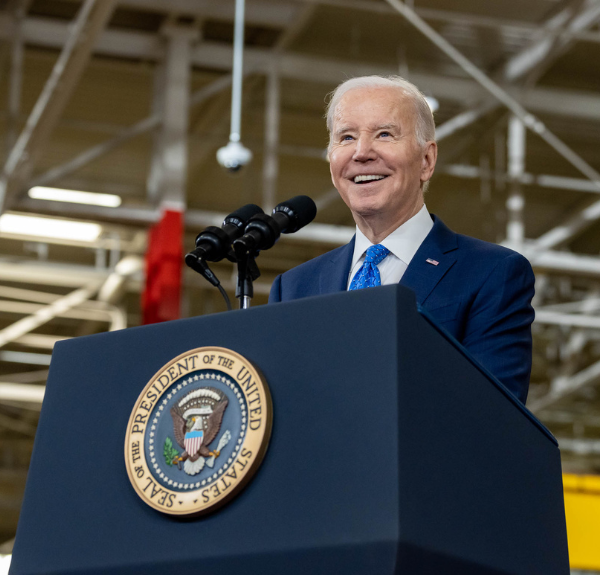 President Joe Biden speaks at a podium in a warehouse.